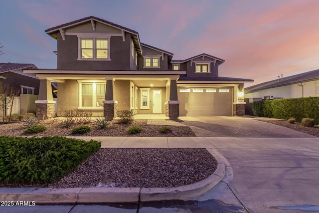 craftsman inspired home featuring decorative driveway, stucco siding, covered porch, an attached garage, and fence