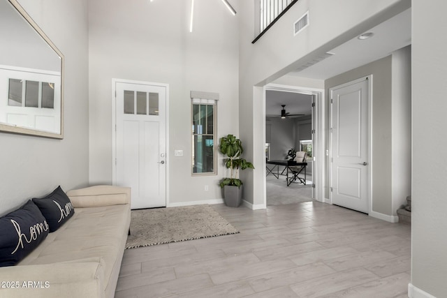 foyer entrance with light wood-style floors, a high ceiling, visible vents, and baseboards