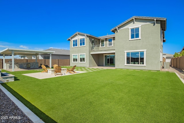 back of house with an outdoor fire pit, a fenced backyard, a yard, and stucco siding