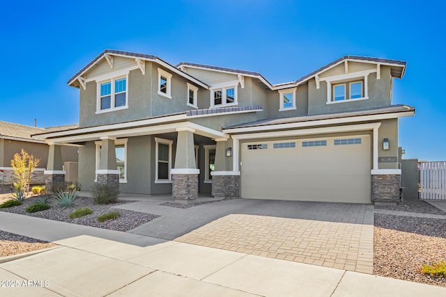 craftsman-style house with a garage, stone siding, fence, decorative driveway, and stucco siding