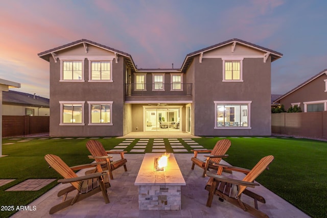 back of house at dusk featuring a fire pit, a lawn, a balcony, fence, and a patio area