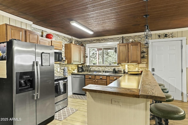 kitchen featuring sink, hanging light fixtures, stainless steel appliances, kitchen peninsula, and a breakfast bar