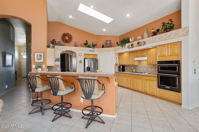 kitchen featuring light brown cabinetry, appliances with stainless steel finishes, a kitchen bar, and light tile patterned floors