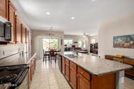 kitchen with stainless steel microwave, open floor plan, light countertops, a center island with sink, and brown cabinetry