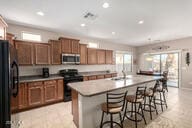 kitchen featuring freestanding refrigerator, a kitchen island with sink, a kitchen bar, stainless steel microwave, and range with gas stovetop
