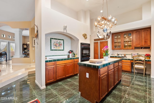 kitchen featuring a kitchen island, tile countertops, a high ceiling, decorative columns, and a notable chandelier