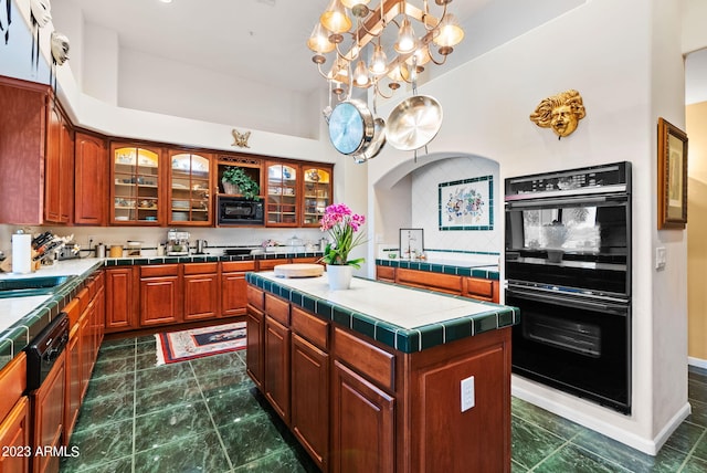 kitchen featuring tile counters, a kitchen island, an inviting chandelier, decorative backsplash, and black double oven