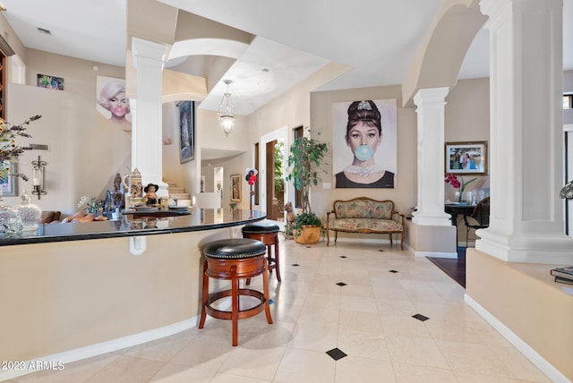 kitchen featuring hanging light fixtures, decorative columns, light tile patterned floors, and a kitchen bar