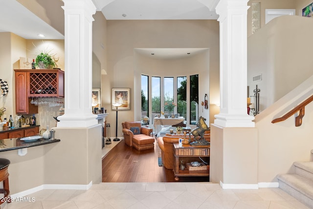 living room featuring light wood-type flooring, decorative columns, and indoor bar