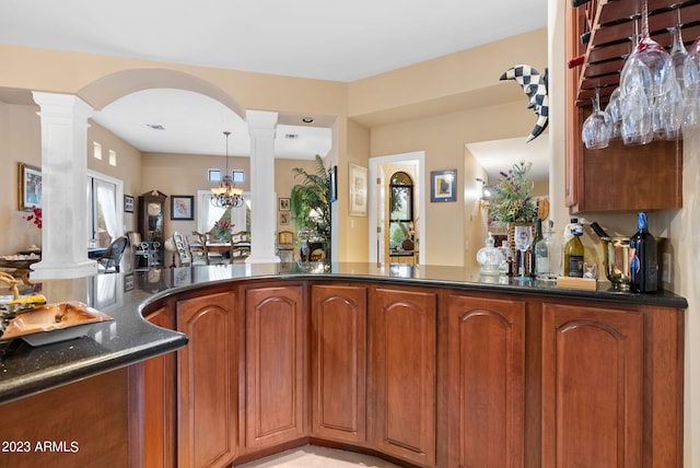 kitchen featuring a notable chandelier, kitchen peninsula, decorative columns, and dark stone counters