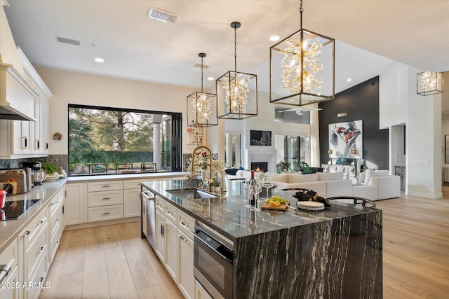 kitchen featuring decorative light fixtures, sink, dark stone counters, a large island, and light hardwood / wood-style floors