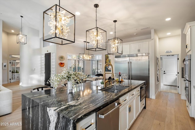 kitchen with stainless steel appliances, white cabinetry, decorative light fixtures, dark stone counters, and a large island