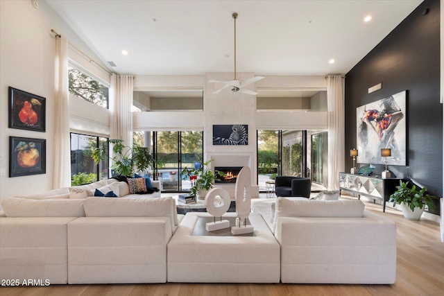 living room with a large fireplace, a towering ceiling, and light wood-type flooring