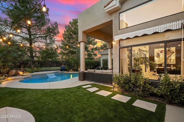 pool at dusk with a patio, outdoor lounge area, a yard, and pool water feature