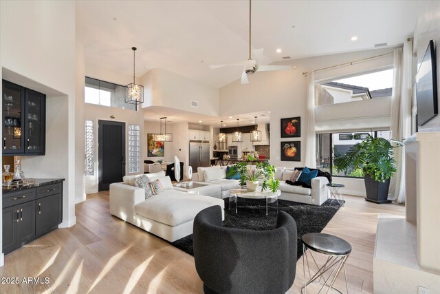 living room with ceiling fan, plenty of natural light, high vaulted ceiling, and light hardwood / wood-style floors