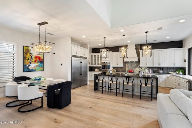 kitchen featuring stainless steel built in refrigerator, white cabinetry, a kitchen breakfast bar, custom range hood, and a kitchen island with sink