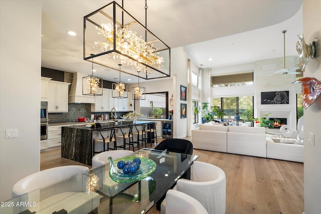 dining room with a large fireplace, beverage cooler, an inviting chandelier, and light hardwood / wood-style flooring