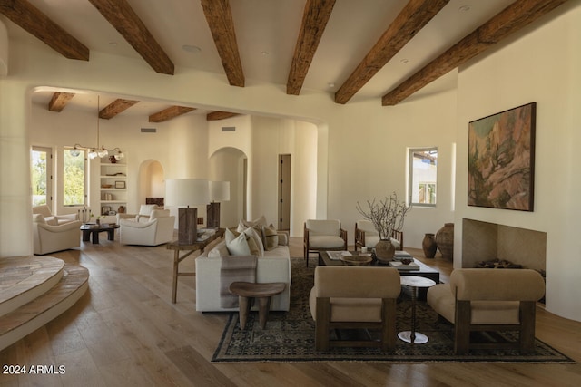 living room featuring built in features, wood-type flooring, beamed ceiling, and a notable chandelier