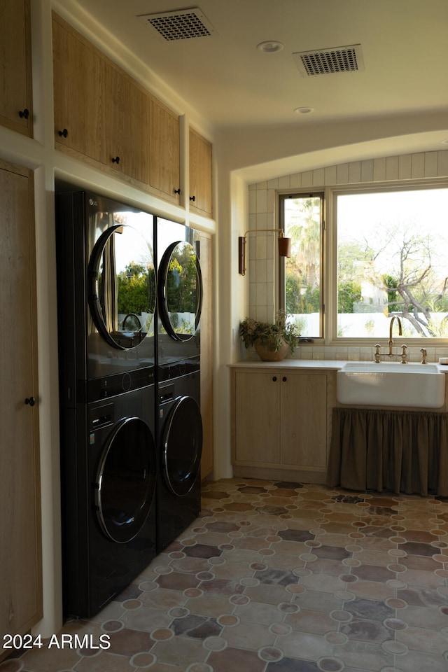 clothes washing area with sink, cabinets, tile floors, and stacked washing maching and dryer