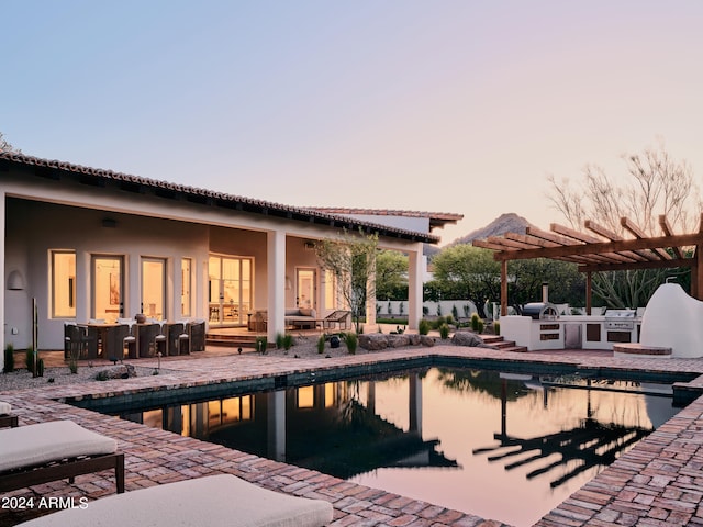 pool at dusk featuring a patio and an outdoor kitchen