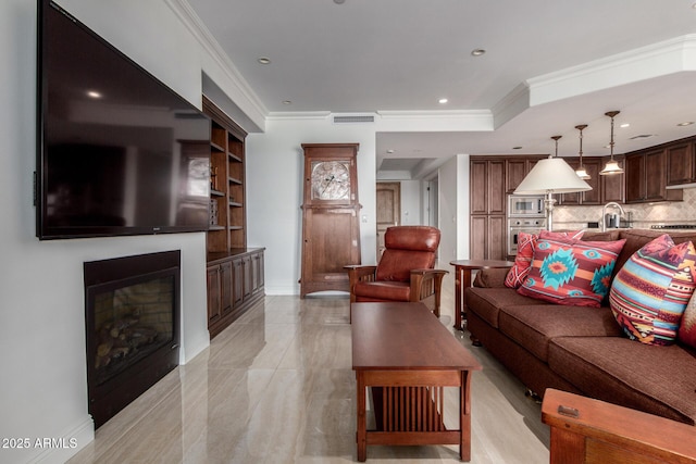 living room featuring a glass covered fireplace, visible vents, ornamental molding, and recessed lighting