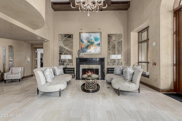 living room with a notable chandelier, a towering ceiling, baseboards, and a premium fireplace