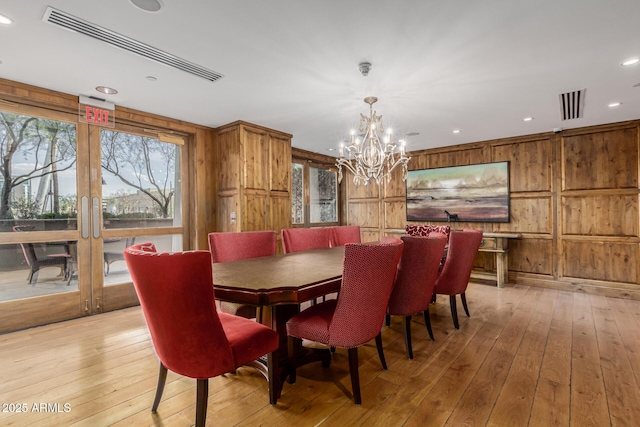 dining room with a notable chandelier, visible vents, light wood-type flooring, and wood walls