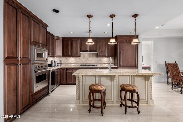 kitchen with light stone countertops, a center island with sink, a breakfast bar, dark brown cabinetry, and appliances with stainless steel finishes