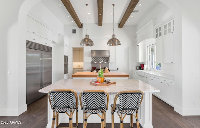 kitchen with pendant lighting, beam ceiling, a center island, and built in appliances