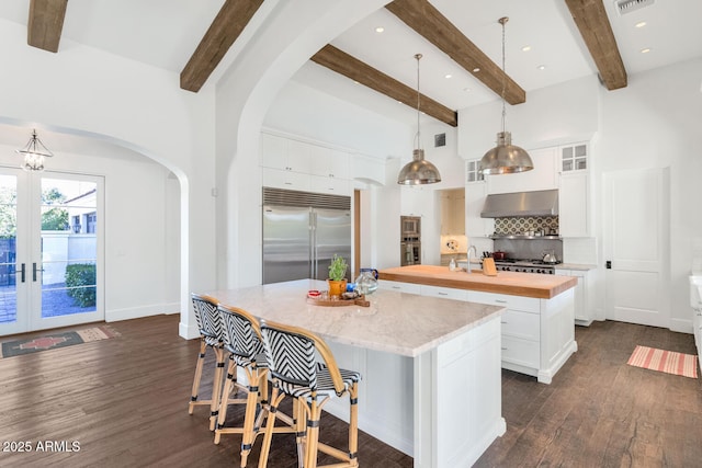 kitchen featuring pendant lighting, a kitchen island, built in appliances, white cabinets, and butcher block counters