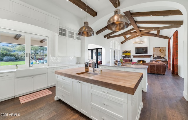 kitchen featuring white cabinets, wooden counters, sink, backsplash, and a kitchen island with sink