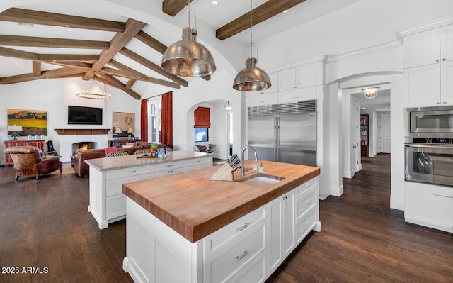 kitchen with white cabinets, decorative light fixtures, built in appliances, an island with sink, and sink