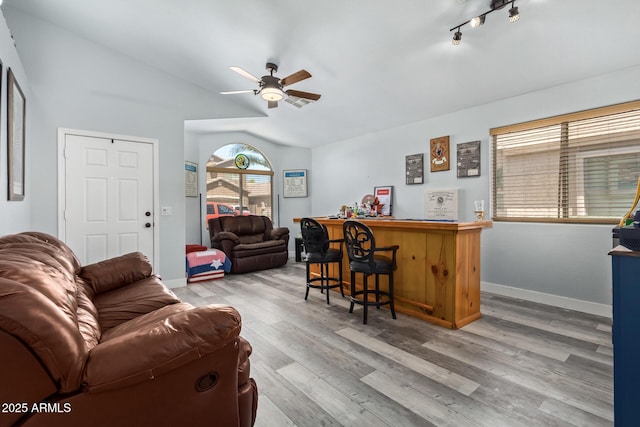 living room with ceiling fan, light hardwood / wood-style floors, bar, and vaulted ceiling