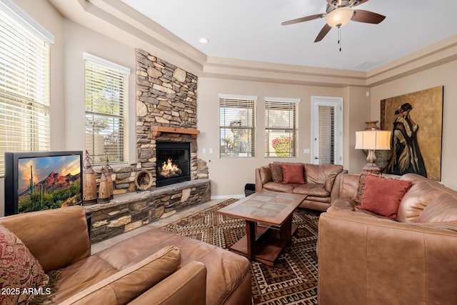 living room featuring a raised ceiling, ceiling fan, and a fireplace