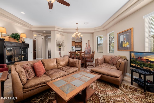 living room featuring a tray ceiling, ceiling fan with notable chandelier, and a wealth of natural light