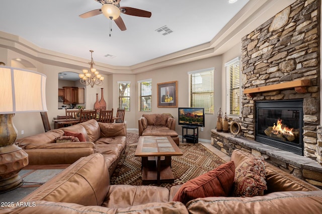 living room with a tray ceiling, a stone fireplace, and ceiling fan with notable chandelier