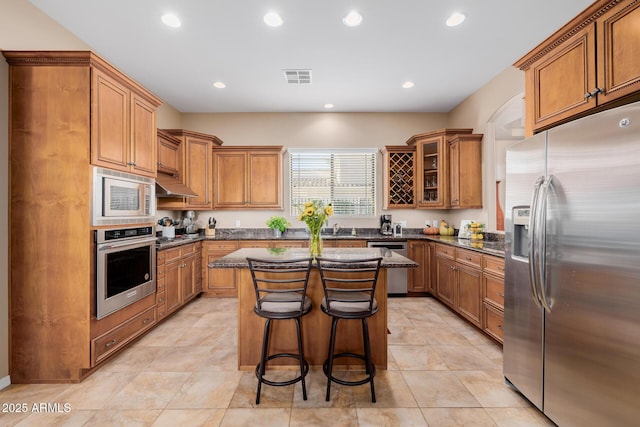 kitchen featuring light tile patterned floors, appliances with stainless steel finishes, dark stone countertops, a kitchen breakfast bar, and a kitchen island