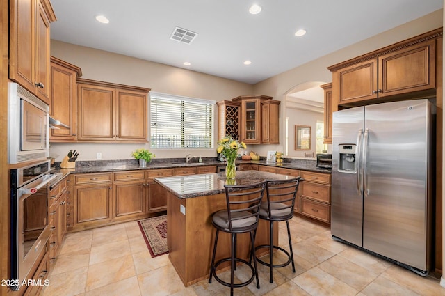 kitchen featuring sink, appliances with stainless steel finishes, dark stone countertops, a kitchen breakfast bar, and a kitchen island