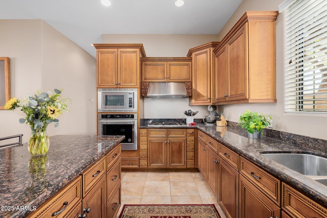 kitchen with stainless steel appliances, exhaust hood, light tile patterned floors, and dark stone counters