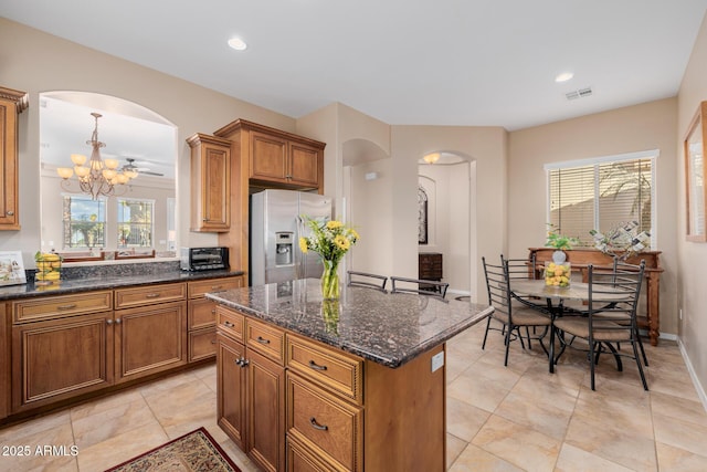 kitchen featuring dark stone countertops, stainless steel fridge with ice dispenser, a center island, and a chandelier