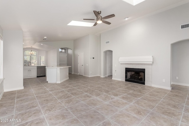 unfurnished living room with ceiling fan, a fireplace, vaulted ceiling, and light tile patterned floors