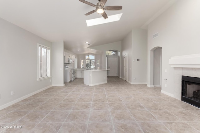 unfurnished living room featuring a tiled fireplace, light tile patterned floors, vaulted ceiling with skylight, and ceiling fan