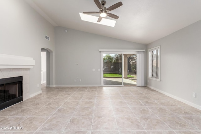 unfurnished living room with ceiling fan, a fireplace, light tile patterned floors, and lofted ceiling with skylight