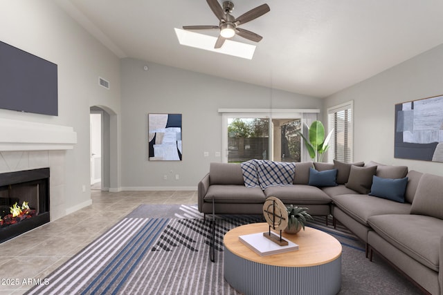 tiled living room with a tile fireplace, lofted ceiling with skylight, and ceiling fan