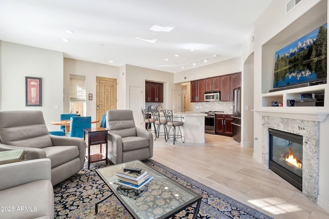 living room with light hardwood / wood-style floors, rail lighting, and a high end fireplace