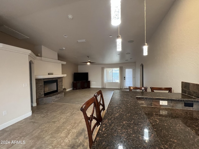 kitchen featuring ceiling fan, decorative light fixtures, a stone fireplace, and dark stone countertops