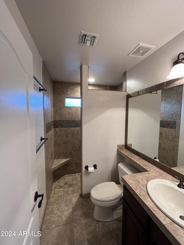 bathroom with tiled shower, vanity, and toilet