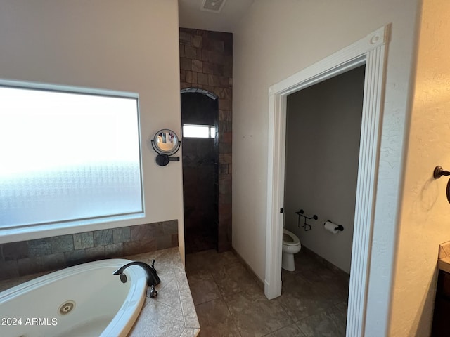 bathroom with a relaxing tiled tub, tile patterned floors, and toilet