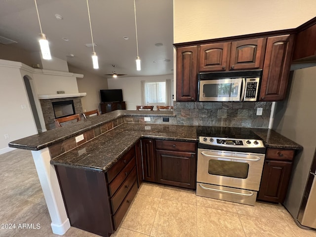 kitchen featuring appliances with stainless steel finishes, decorative light fixtures, kitchen peninsula, and dark stone countertops