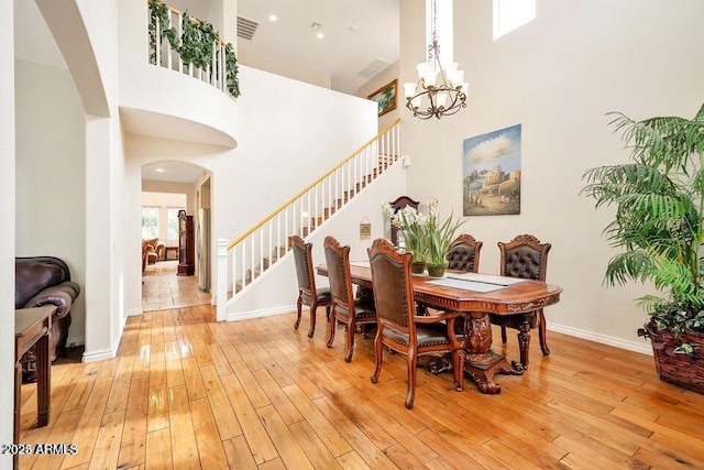 dining room featuring a notable chandelier, a towering ceiling, and light hardwood / wood-style flooring